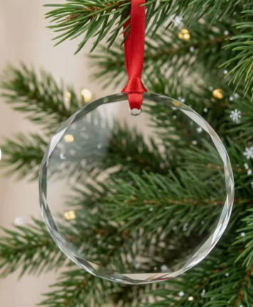 Personalized engraved crystal Christmas ornament with a faceted edge, hanging from a red ribbon on a pine branch